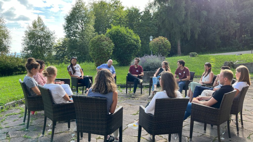 Gruppe sitzt auf Terrasse vor Tagungsraum im Kreis